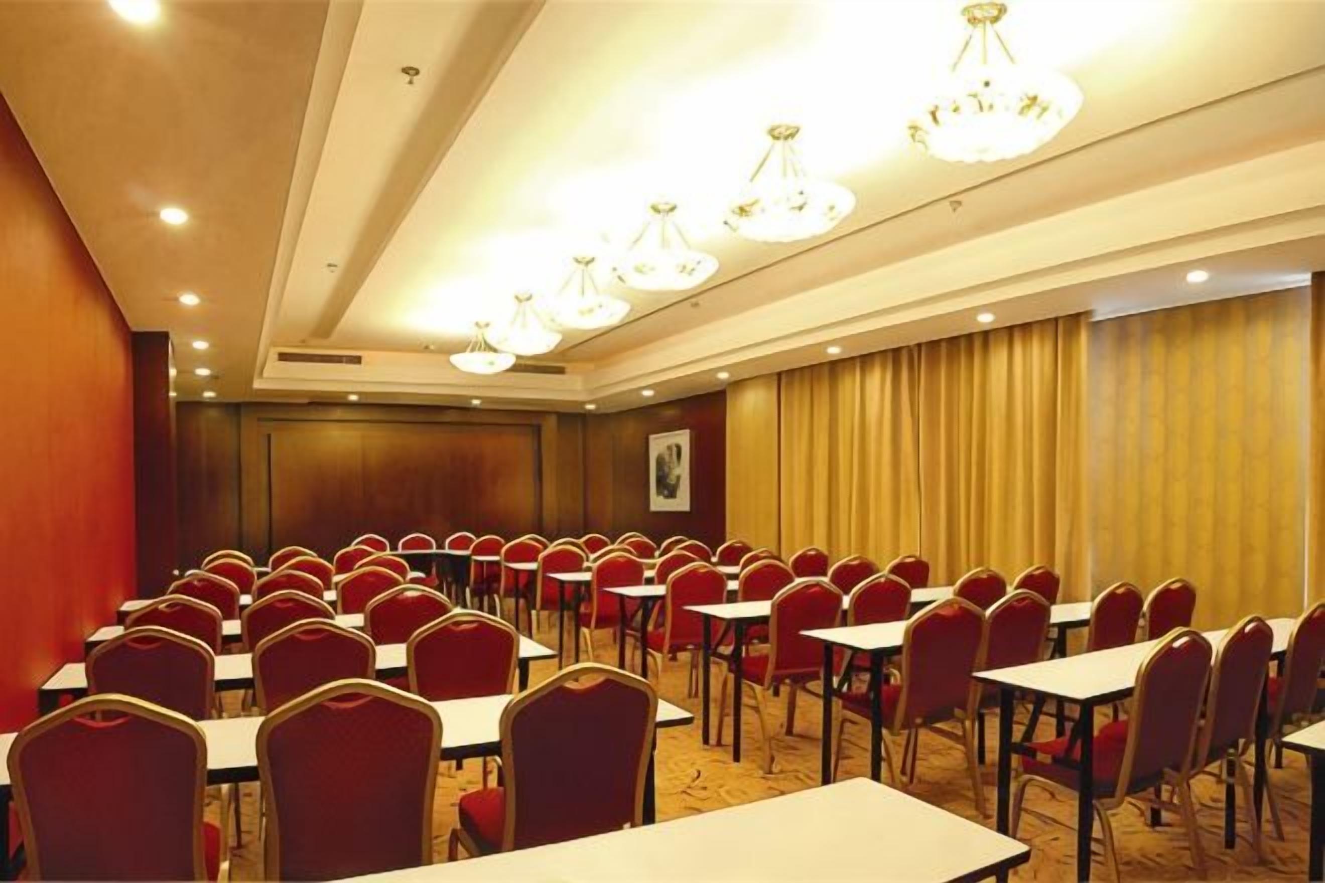 Un salón de conferencias con filas de mesas y sillas, una araña y un cuadro en la pared.