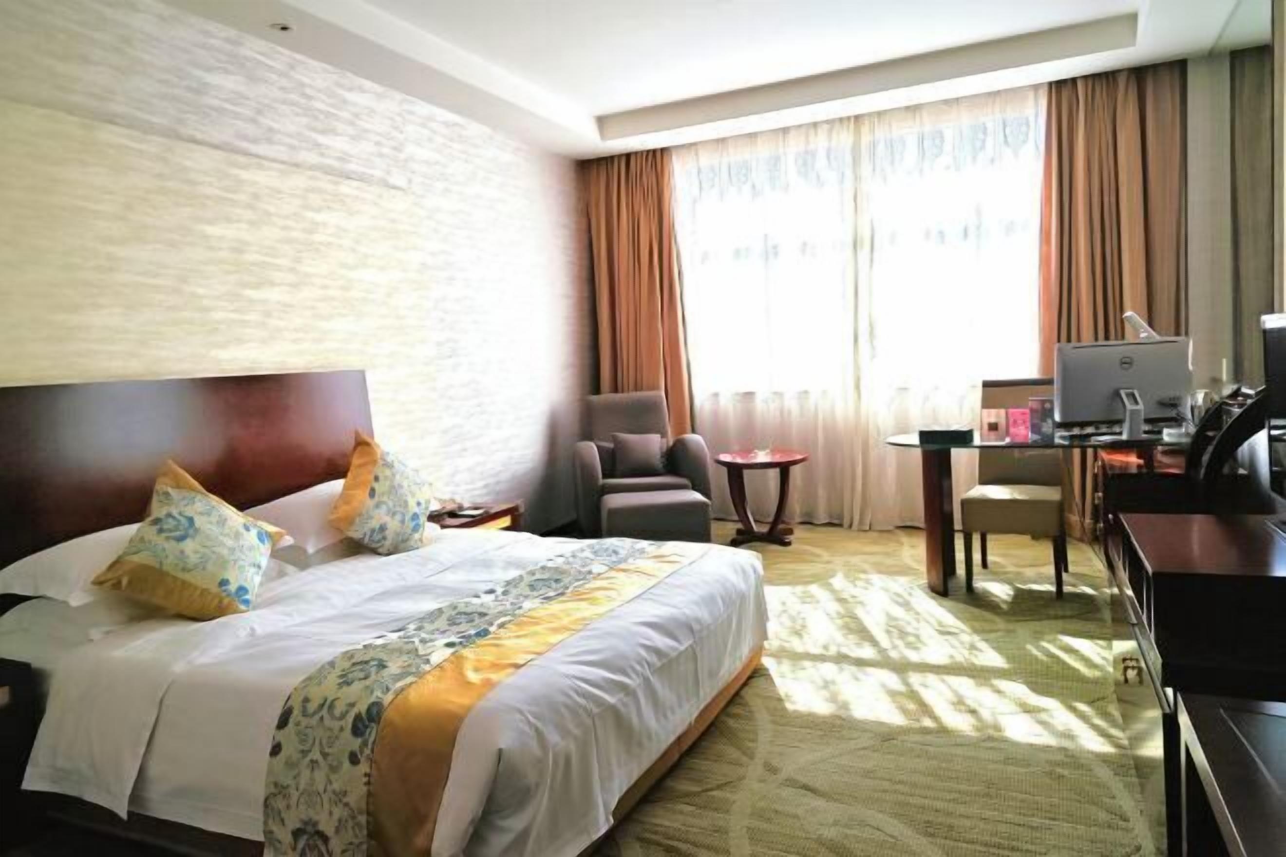 A hotel room with a large bed, a desk with a computer, a chair, and a small table.