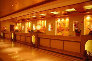 A hotel reception area with a long counter, multiple light fixtures, and decorative elements. - Taitan International Hotel (Xinchang)