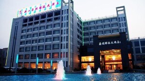 A hotel with a large sign on the top, a fountain in front, and a well-lit entrance. - Taitan International Hotel (Xinchang)