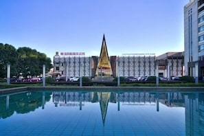 Un hotel con piscina reflectante, una estructura triangular destacada y varios edificios al fondo.