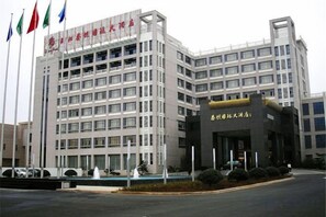 A multi-story building with a prominent entrance and flags. - Taitan International Hotel (Xinchang)
