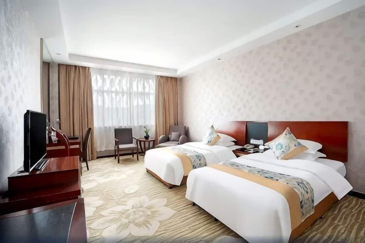 A hotel room with two beds, a TV, a desk, and a chair.