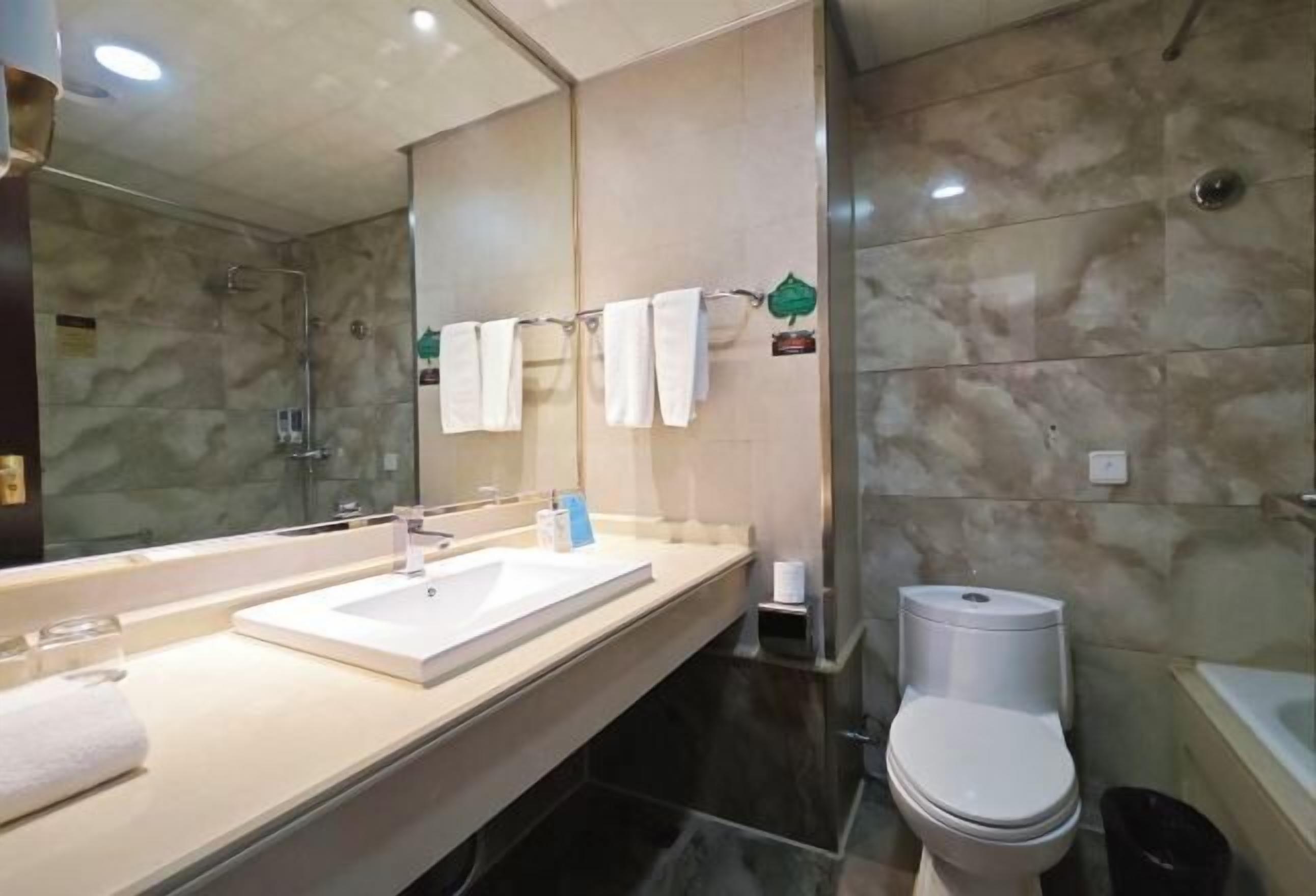 A modern bathroom with a marble wall, a large mirror, a sink, a toilet, and a shower area.