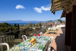 A balcony with a table set for two, overlooking a scenic view of the sea and mountains.