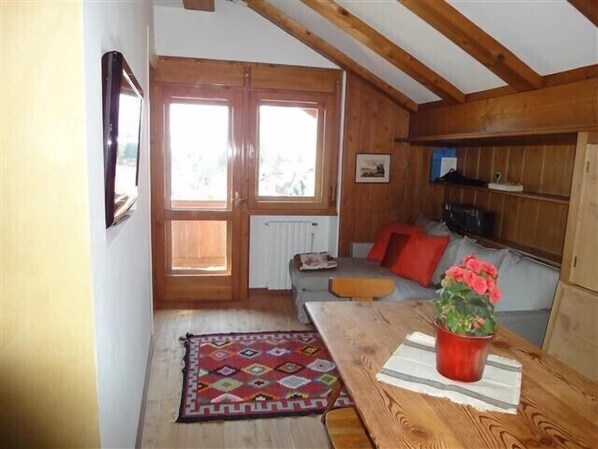 Une pièce chaleureuse avec un plafond en bois, une table à manger agrémentée d’un vase de fleurs, un canapé avec des coussins rouges et une fenêtre offrant une belle vue.