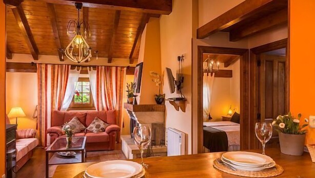 Una habitación acogedora con techo de madera, un sofá, una mesa de comedor para dos personas y una chimenea.
