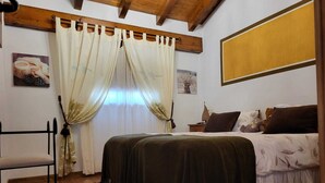 Un dormitorio con cama, mesita de noche, silla y cortinas.
