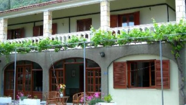 A two-story building with a balcony, arched windows, and a garden area with chairs and tables. - APARTMENT FOR 6 PERSONS AT THE CENTER OF BARBATI, 50 METERS FROM THE BEACH (Corfu)