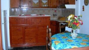 A kitchen with wooden cabinets, a tiled backsplash, and a dining area with a table set for two. - APARTMENT FOR 6 PERSONS AT THE CENTER OF BARBATI, 50 METERS FROM THE BEACH (Corfu)