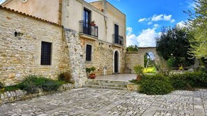 A stone building with a courtyard, featuring a balcony with a railing, a door, and a window. - Carizza Country Luxury Villa (Rosolini)