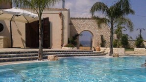 A clear swimming pool with steps leading into it, surrounded by a stone wall and palm trees. - Carizza Country Luxury Villa (Rosolini)