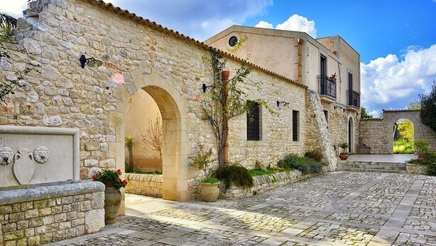 A stone building with a courtyard, featuring a stone wall, an archway, and a potted plant. - Carizza Country Luxury Villa (Rosolini)