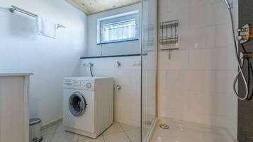 Une salle de bain compacte équipée d’un lave-linge, d’une douche à parois de verre et d’une fenêtre laissant entrer la lumière naturelle.