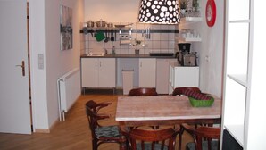 A compact kitchen with white cabinets, a dining table with chairs, a hanging pot rack, and a coffee machine.