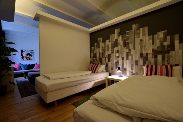 A modern hotel room with a large bed, a smaller sofa, a desk with a lamp, and a decorative wall panel.