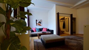 A living room with a sofa, ottoman, and a large plant.