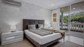 A modern bedroom with a large bed, a nightstand, and a view of a balcony with a railing. - Modern holiday villa with sea and panoramic views (Provensals)
