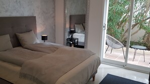 A bedroom with a large bed, a nightstand, a lamp, a chair, and a view of a garden through a glass door. - Modern holiday villa with sea and panoramic views (Provensals)