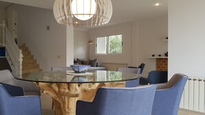 A modern dining area with a glass-top table, blue upholstered chairs, and a unique wooden centerpiece. - Modern holiday villa with sea and panoramic views (Provensals)