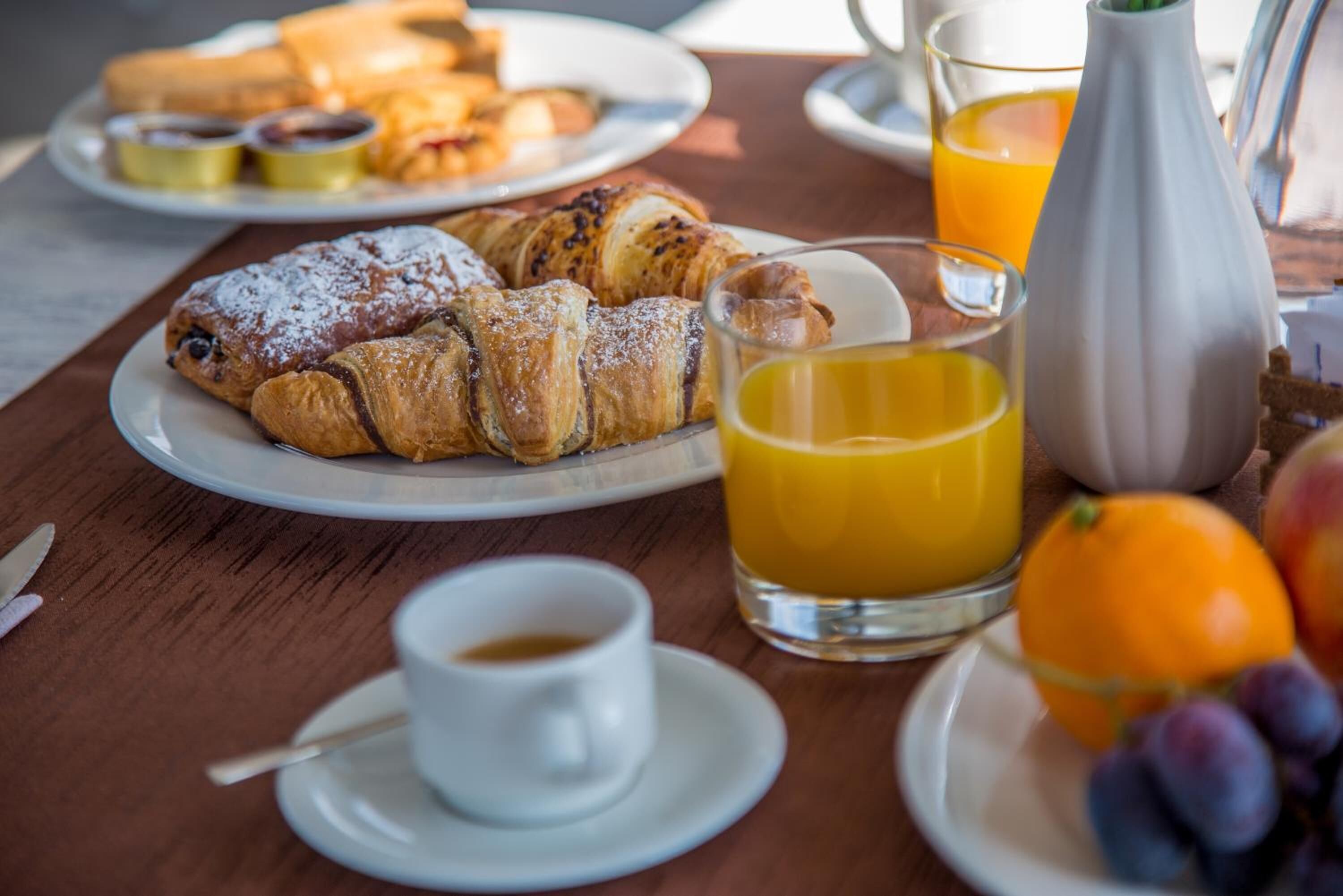 A breakfast setting with croissants, orange juice, and a cup of coffee on a wooden table.
