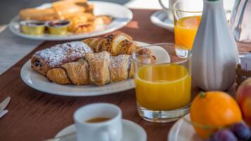 A breakfast setting with croissants, orange juice, and a cup of coffee on a wooden table.