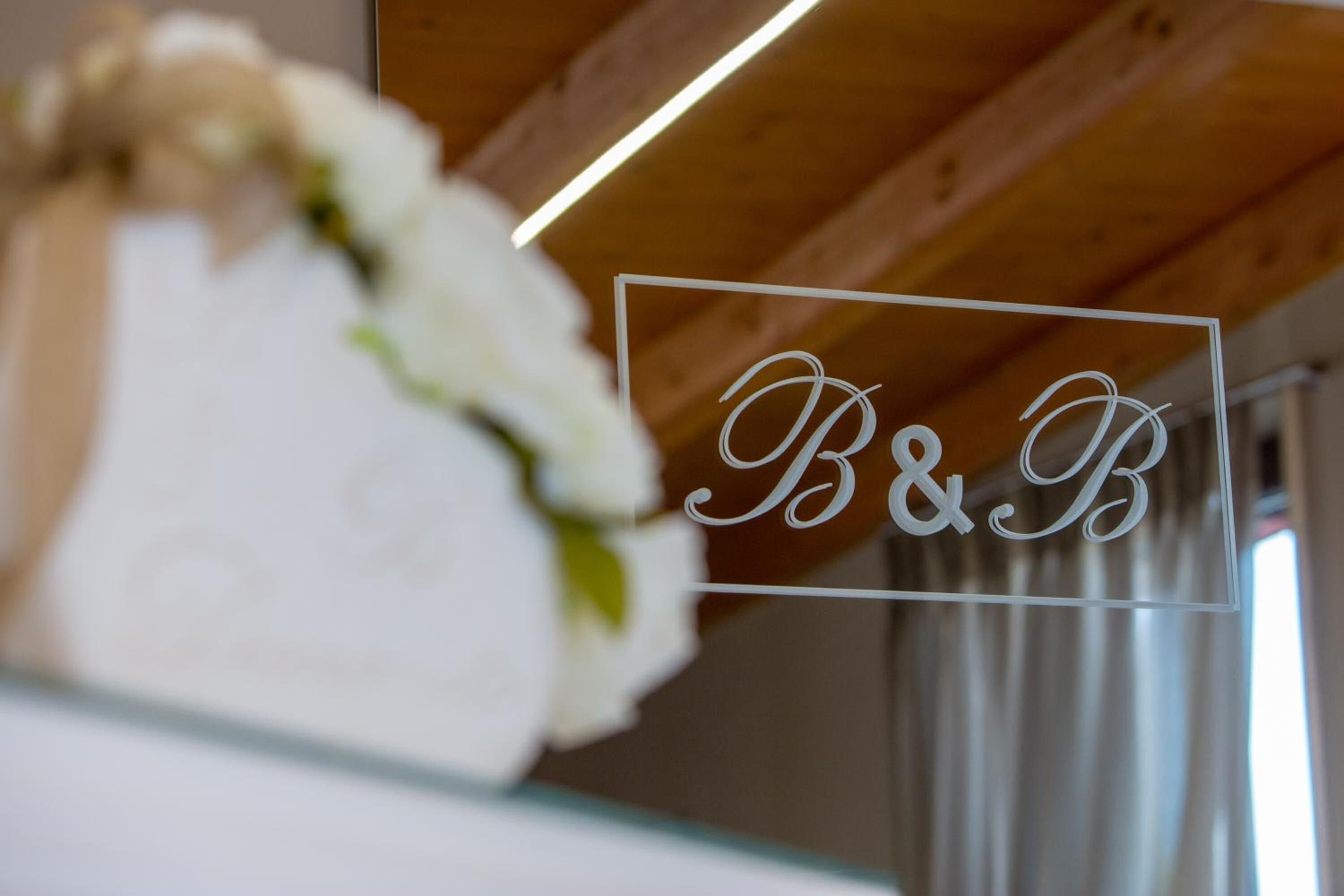 A framed sign with the initials "B&B" in a decorative font, hanging on a wooden beam.