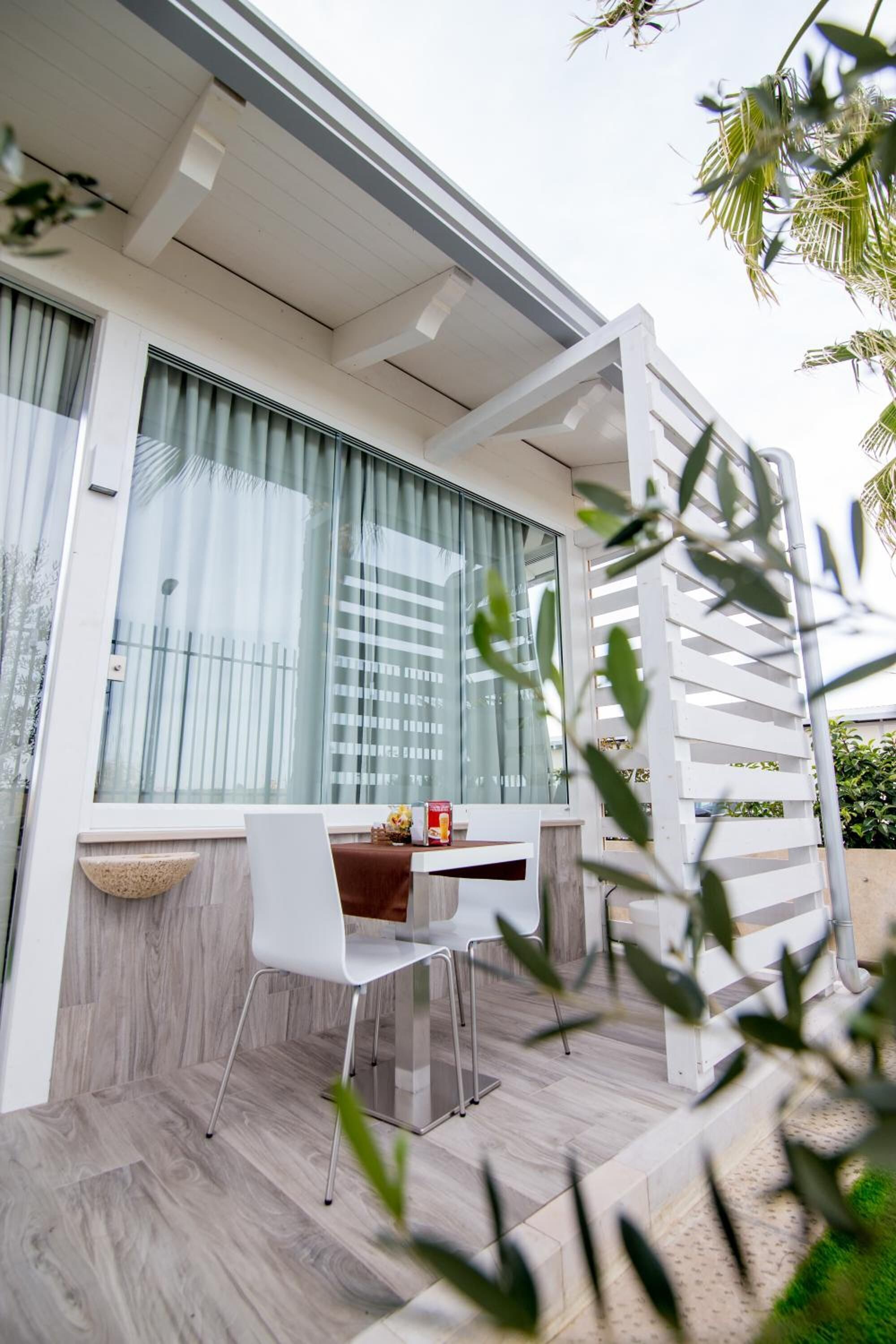 Un área de estar moderna al aire libre con una mesa y sillas blancas, un cuenco decorativo pequeño y una estructura de pérgola blanca.