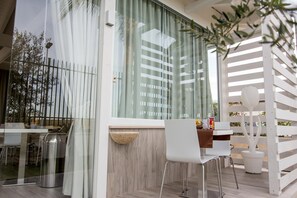 Un espace extérieur moderne, aménagé avec une table en verre, des chaises blanches et une clôture en bois peinte en blanc.