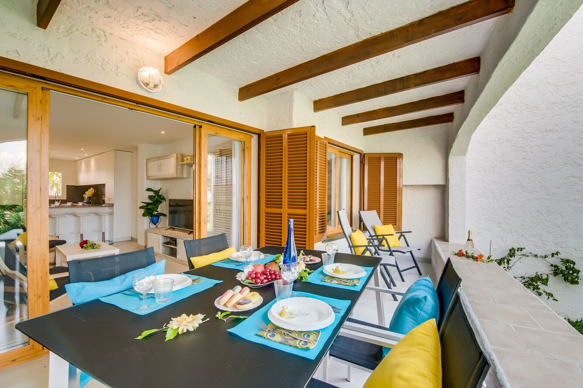 Een eethoek met een tafel gedekt voor vier personen, een keuken achtergrond en houten balken in het zichtbare plafond.