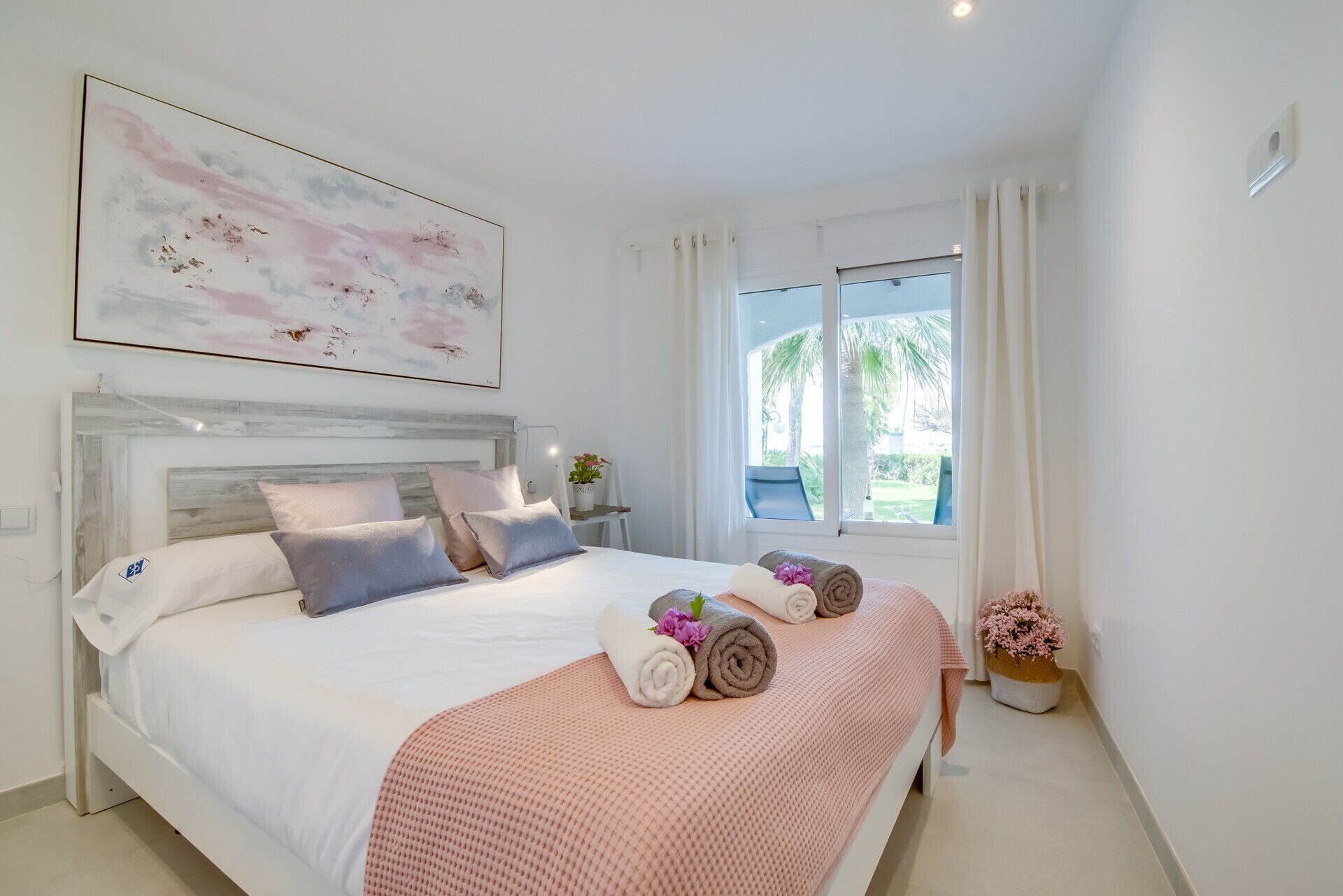 Een moderne slaapkamer met een groot bed, een hoofdeinde, een raam met gordijnen en een schilderij aan de muur.