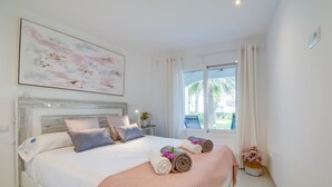 A modern bedroom with a large bed, a headboard, a window with curtains, and a painting on the wall.