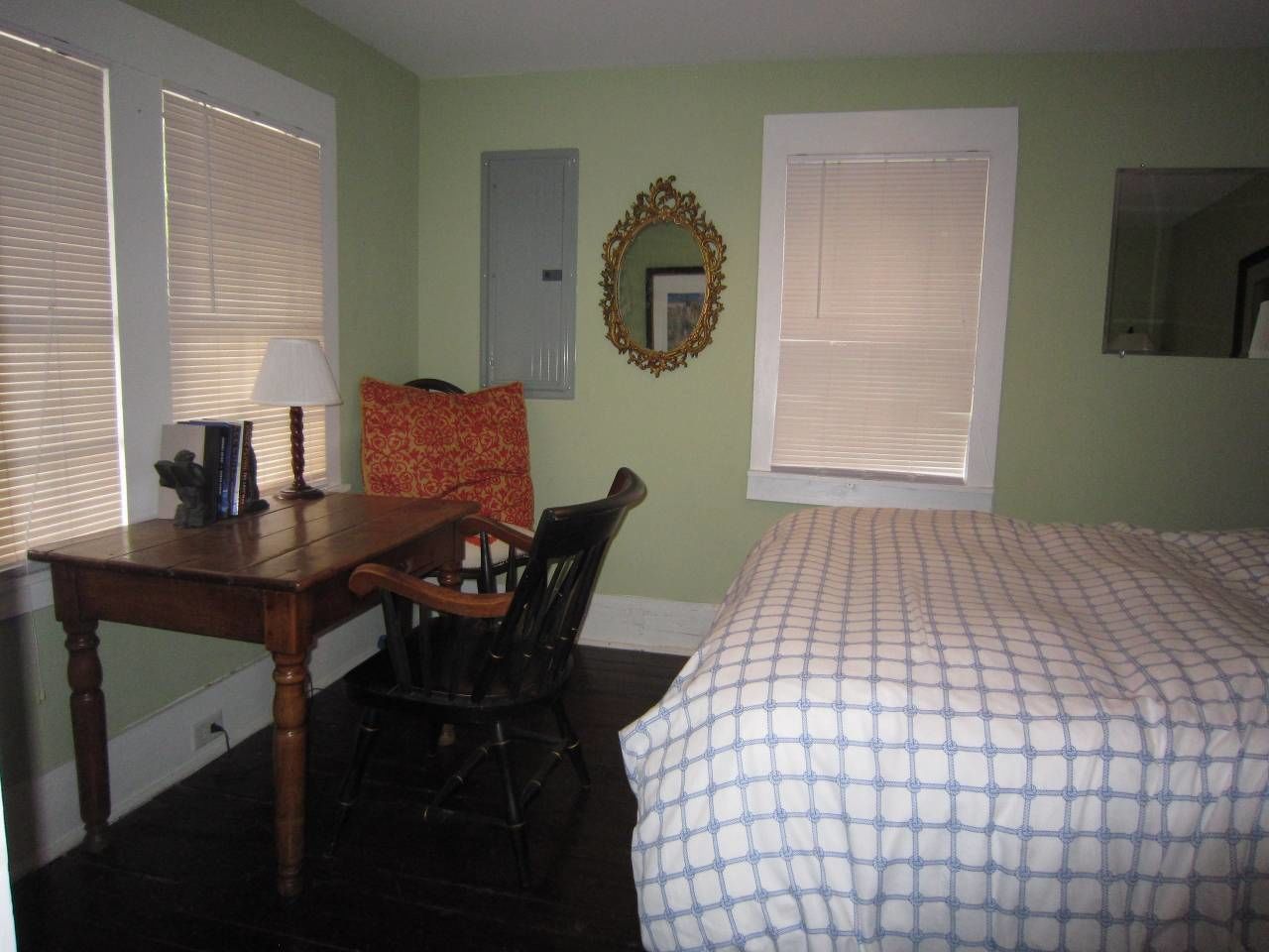 Un dormitorio con cama, escritorio, silla, espejo y ventana con persianas.