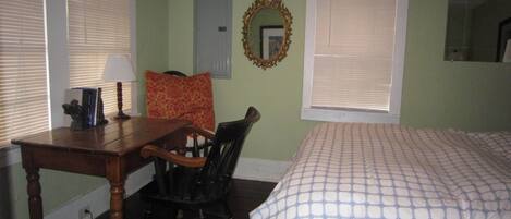 Un dormitorio con cama, escritorio, silla, espejo y ventana con persianas.