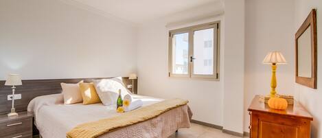A bedroom with a bed, bedside tables, a window, a wooden dresser, and a lamp.