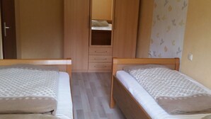Ein Zimmer mit zwei Holzbetten, einem Kleiderschrank und einer kleinen Ablagefläche.