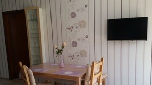 Ein Essbereich mit Holztisch und -stühlen, einer Vase mit Blumen und einem an der Wand montierten Fernseher.