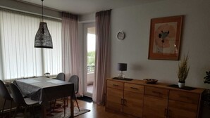 Un coin repas avec une table dressée pour quatre personnes, un meuble en bois, un luminaire suspendu et un tableau encadré au mur.