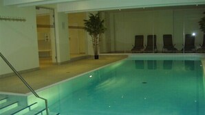 Ein beheizter Innenpool mit klarem Wasser, eine Treppe, die zum Pool führt, und mehrere Liegestühle am Pool.