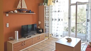 Ein Wohnzimmer mit Fernseher, Holzschränken, einem roten Sofa und einem Balkon mit Blick.
