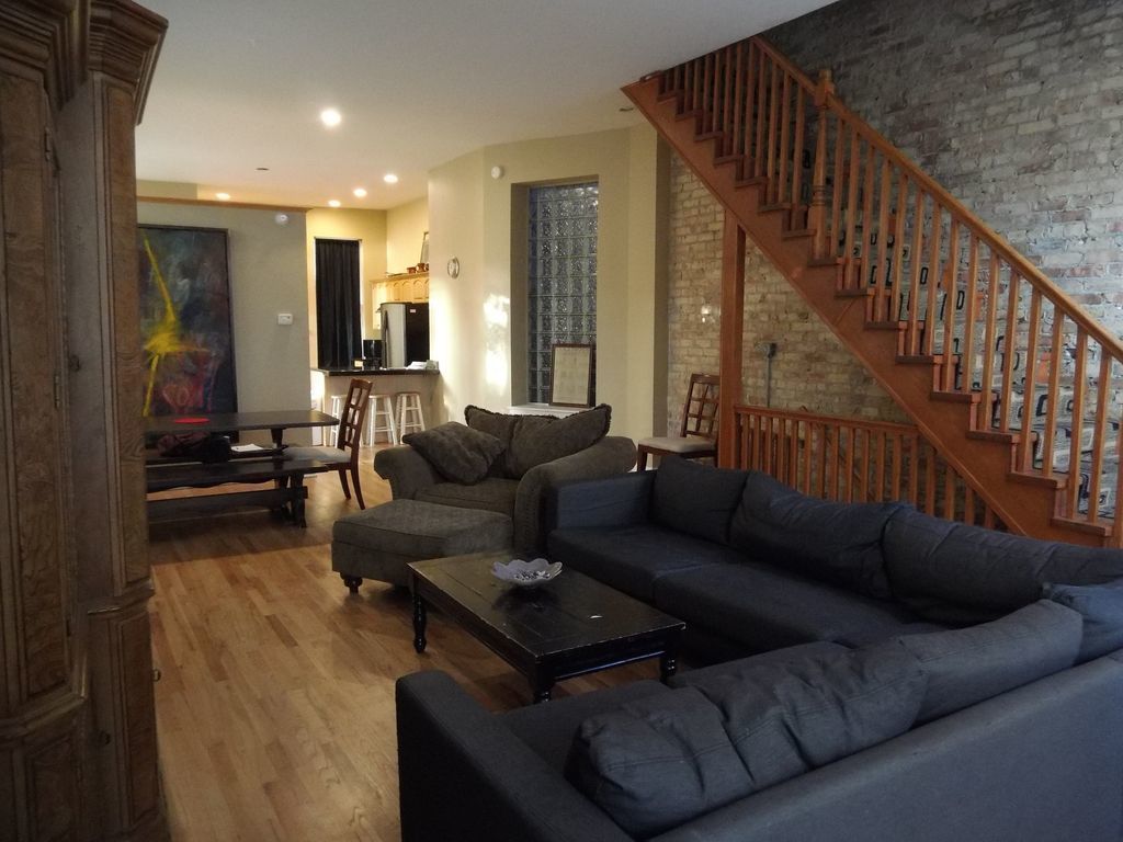 A living room with a wooden staircase, a sofa set, and a dining area.