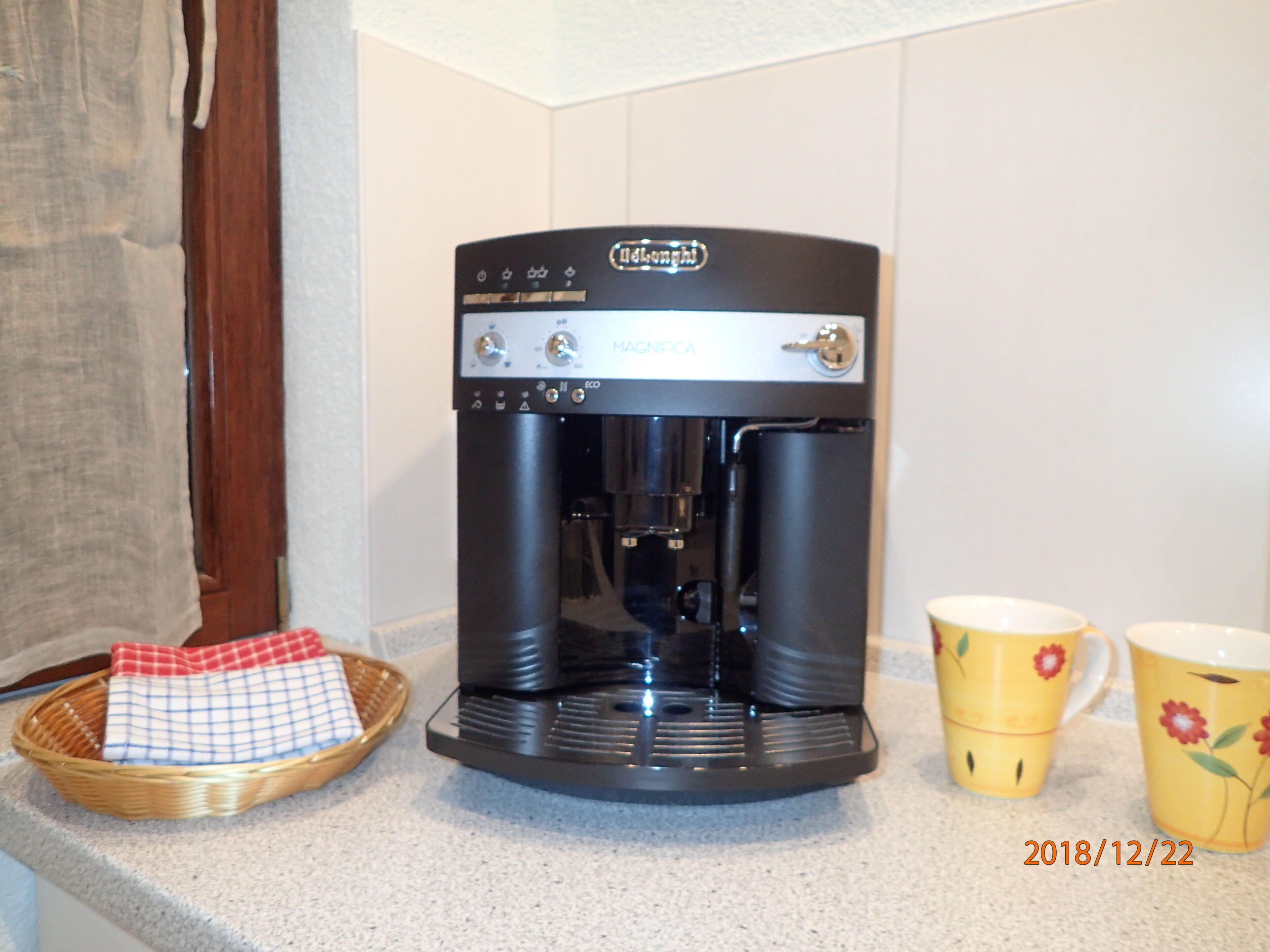 Una cafetera con un panel de control y dos tazas de café sobre una encimera de cocina.
