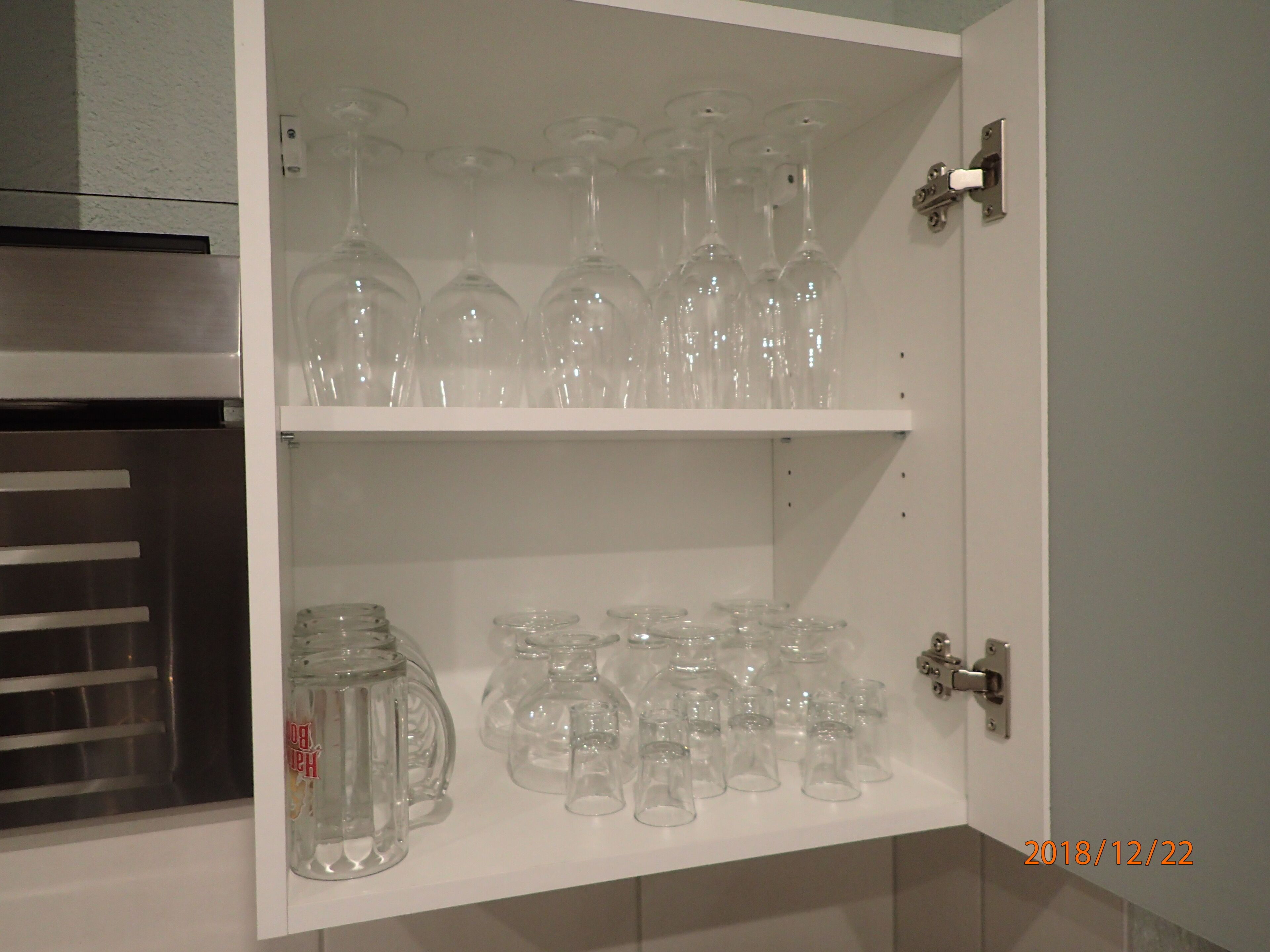 Ein Schrank mit Regalen, auf denen verschiedene Gläser, darunter Weingläser und Bierkrüge, stehen.
