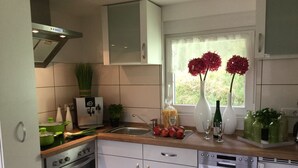 Une cuisine moderne avec des meubles blancs, un four en acier inoxydable, un lave-vaisselle et une fenêtre donnant sur un paysage verdoyant.