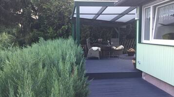 Un patio techado al aire libre con una mesa y sillas, rodeado de abundante vegetación.