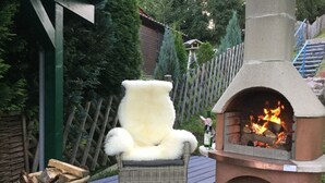 Une terrasse avec un foyer en pierre, un fauteuil en osier et un panier de bois.