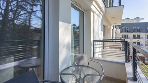 Un balcón con una mesa y sillas de vidrio, vista a la ciudad, y un edificio con balcones.