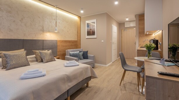 Una habitación de hotel moderna con una cama grande, un área de estar, una pequeña cocina y un baño.