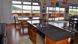 A modern kitchen with a large island, wooden cabinets, and a view of a lake through large windows. - Downtown Condo With Lake & BAY Views (Frankfort)