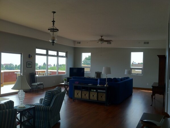 A spacious living room with a blue sectional sofa, a television, and a ceiling fan.